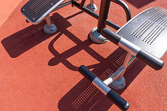Close-up of seamless REGUPOL impact-absorbing safety surfacing and sports surfacing beneath outdoor fitness equipment at an accessible play and recreation area in Berlin-Steglitz-Zehlendorf.