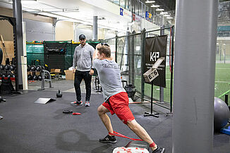 Kelowna High Performance - Training with REGUPOL aktiv Flooring Athlete performs athletic training exercises while a coach supervises the athlete. The Kelowna High Performance facility features REGUPOL aktiv rolled rubber flooring.