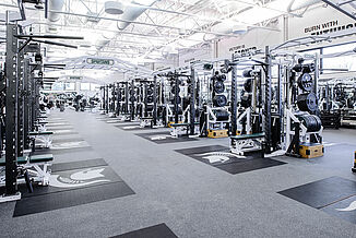 Michigan State Football Weight Room - Row of Weight Racks Rows of weight racks at Michigan State football weight room facility, each featuring an individual, inlaid REGUPOL crash platform with a customized Spartan logo.