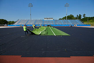Spring Grove Area High School - Unfold of Turf on REGUPOL abzorb Workers unfold the turf onto REGUPOL abzorb at Spring Grove Area High School. A view of the high school stadium is located in the background.