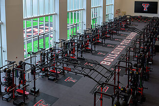 Texas Tech Football - Downward view Downward view of the Texas Tech Football weight room with a full view of squat racks and the view of the outdoor practice field.