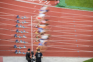 Sprint start at the 2022 European Athletics Championships in Munich – athletes in motion on the red running track. Start of a sprint final at the 2022 European Athletics Championships in Munich’s Olympic Stadium. Athletes explode from the starting blocks on the red synthetic track, captured by camera crews.