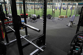 Kelowna High Performance - Weight Training & REGUPOL aktiv Flooring View of a weight rack and equipment at Kelowna High Performance, leading into the turf area of the facility. REGUPOL aktiv rolled rubber flooring is used throughout the non-turf areas of the complex.