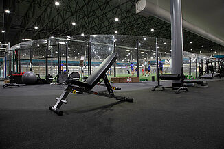 Kelowna High Performance - Weight Bench & REGUPOL aktiv Flooring A inclined weight lifting bench rests on REGUPO aktiv rolled rubber flooring, with a view of the turf area in the background of Kelowna High Performance. There are a number of athletes located on the turf, receiving instruction from a coach.