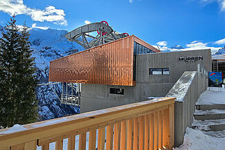 Cable car station from the outside. Snow lies on the steps. A lot of wood was used in the construction of the building.