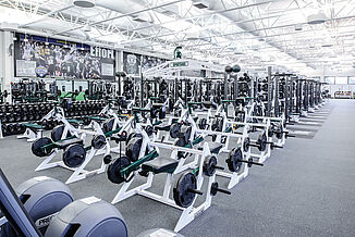 Michigan State Football Weight Room - Machines Offered View of the number of different machine and equipment that are offered to athletes in the Michigan State football weight room. All equipment is positioned on REGUPOL aktivpro roll flooring in Thunder Gray.