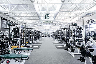 Michigan State Football Weight Room - Length of Room The length of the Michigan State football weight facility, showcasing the vast number of free weights, weight racks and machines throughout. All of the equipment rests on REGUPOL aktivpro roll flooring and REGUPOL crash.
