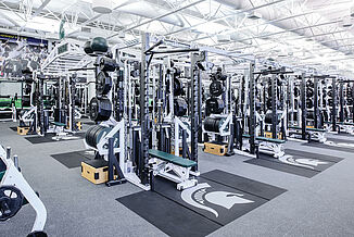 Michigan State Football Weight Room - Weight Racks and Platforms View of the rows of weight racks located at Michigan State's football weight room facility. The racks feature REGUPOL crash zones that seamlessly transition into the REGUPOL aktivpro roll flooring.