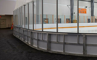 Thayer Sports Center Ice Rink - REGUPOL aktiv Rolled Rubber Flooring Indoor ice rink at Thayer Sports Center with white surface, orange lines, and glass walls, set in a large room with REGUPOL aktiv rubber rolled flooring and white walls.