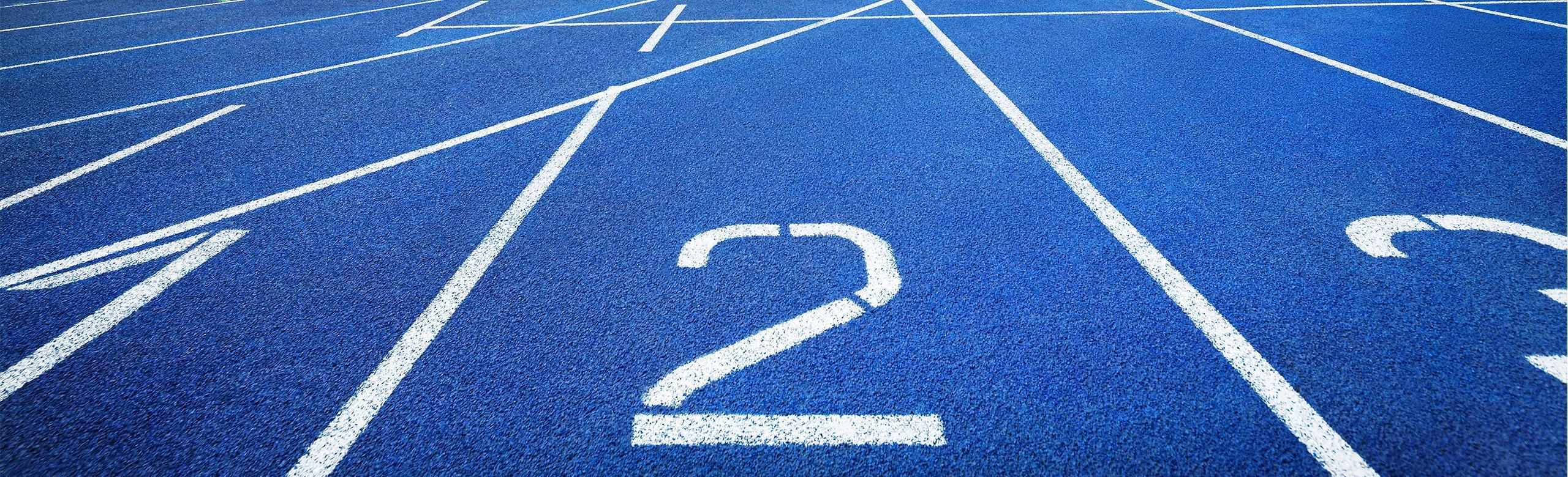 Blue running track with lane markings – slip-resistant and competition-ready. Front view of a blue synthetic running track with white markings and numbered lanes. The surface is slip-resistant and designed for athletics competitions and sprint training.