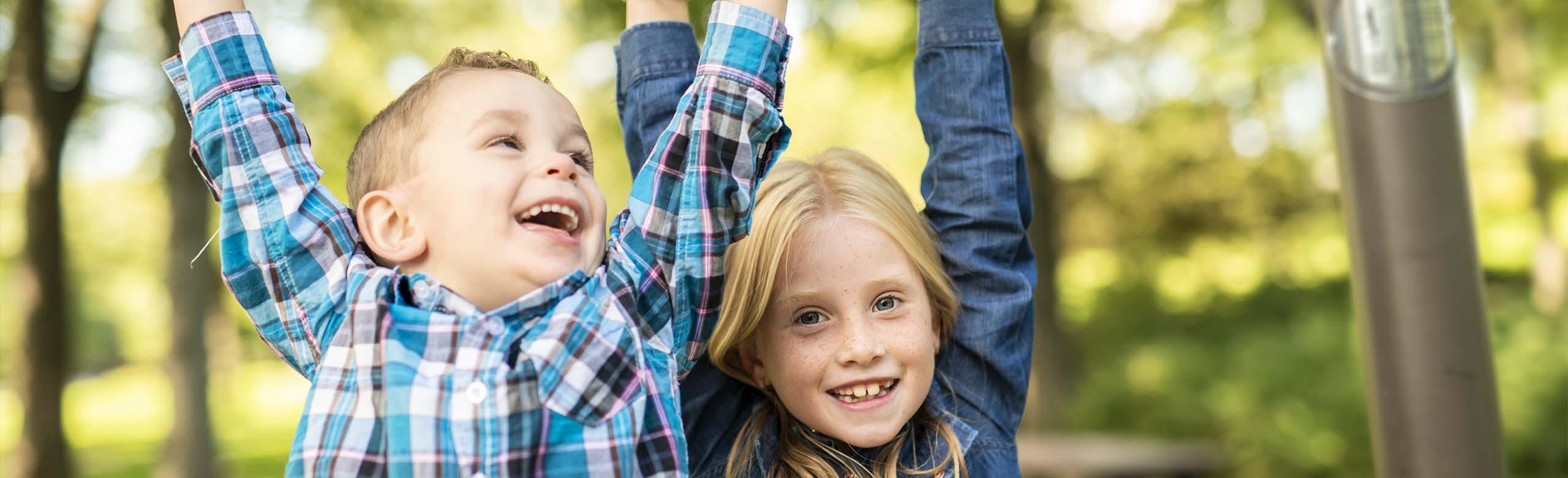 Children play safely on a colourful multifunctional play area with REGUPOL playfix elastic tiles, surrounded by trees.