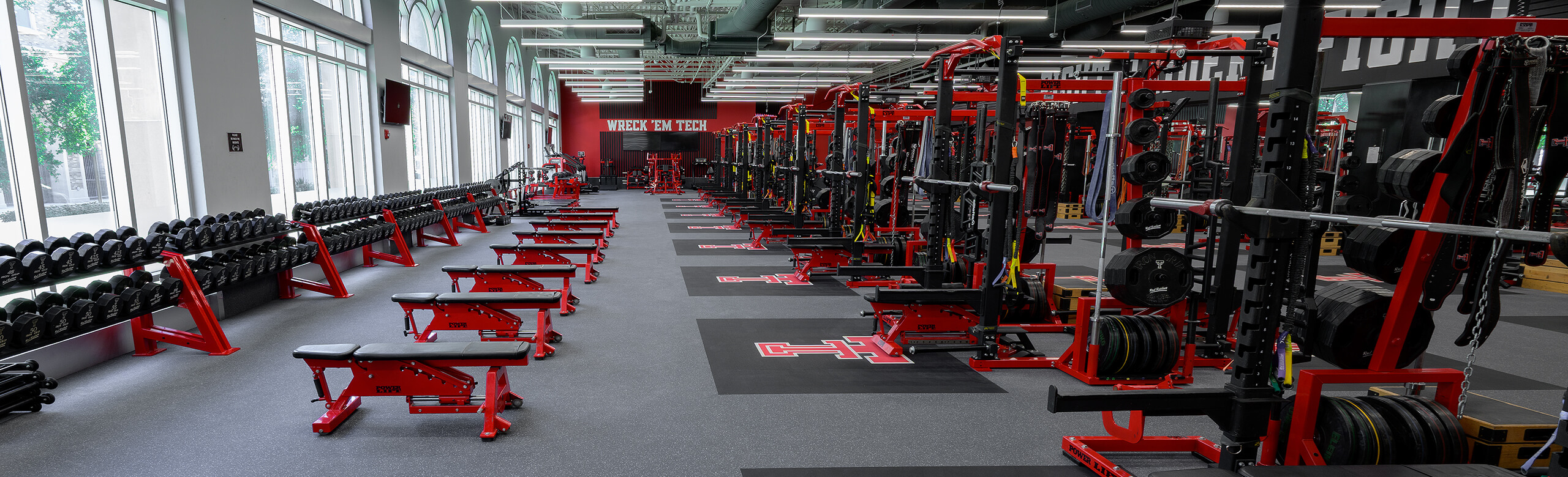 Texas Tech Olympic - Banner View of the side of the Texas Tech Olympic room that features free weights and benches, as well as weight racks.
